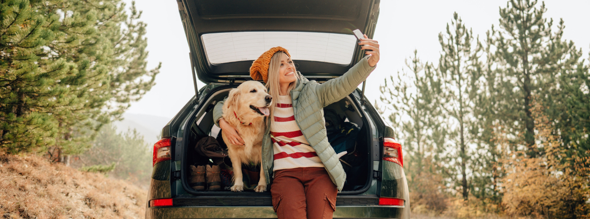 image of woman in a beanie and coat taking a selfie with dog in the back of her car 