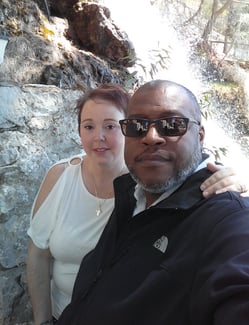 Husband and wife posing in front of a waterfall in Greece