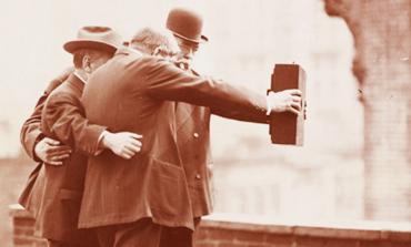 Three well-dressed gentleman standing on a rooftop. 1920 era. Warm sepia tone.
