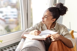 woman staring out window while journaling